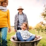 A grandfather wheels his smiling granddaughter in a wheelbarrow