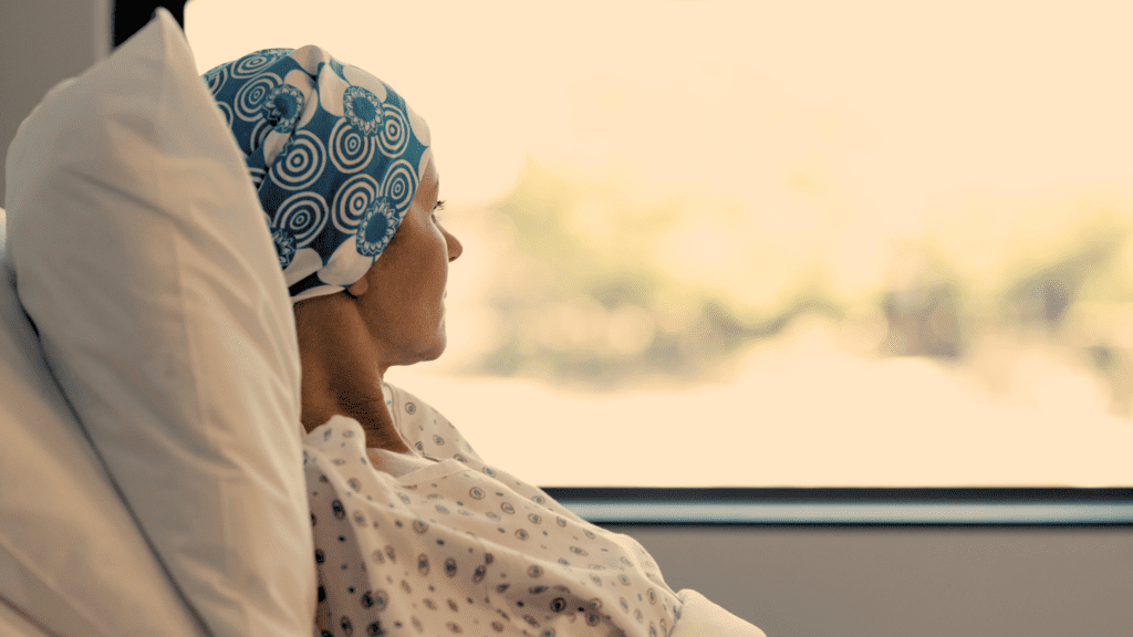 A woman experiencing cancer fatigue, lying down in bed, looking out the window.